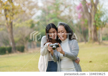 Asian teenage mother and daughter walking in park with camera to capture memories. 104659625