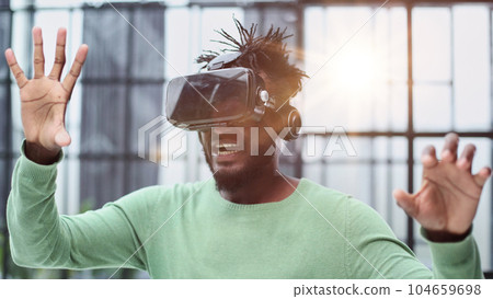 Cool handsome african american man put on virtual reality goggles for the first time in the office. 104659698