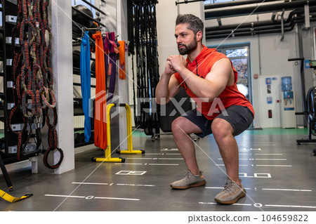 Athletic man warming up and stretching legs doing sit-ups before training fitness gym, body care 104659822
