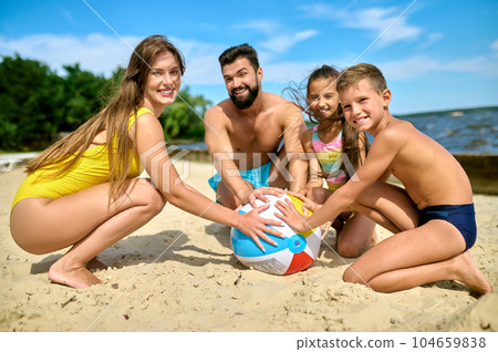 Mother father son and daughter playing inflatable ball on sand by river in summer. Mother father son and daughter playing inflatable ball on sand by river in summer. 104659838