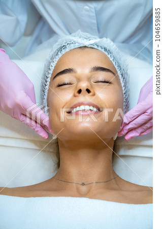 Female beautician doctor cleaning customer skin, make facial massage to patient. 104659885