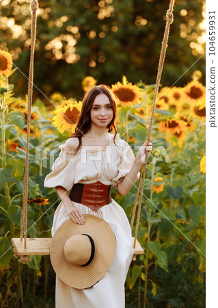 Woman in a dress in a field of sunflowers on a swing 104659931