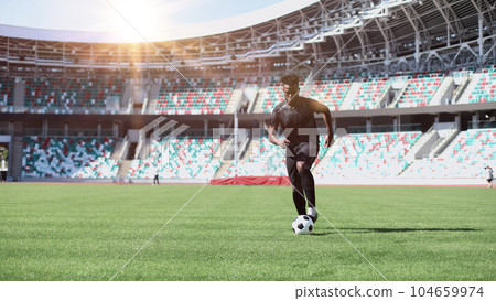 African American man playing football on the stadium field. A man runs with a soccer ball across the field. African American man playing football on the stadium field. A man runs with a soccer ball across the field. 104659974