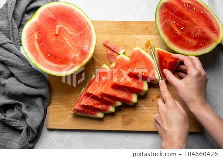 Female hands cutting fresh juicy watermelon slices on cutting board. 104660426