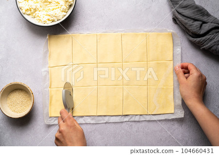 Cutting raw puff pastry dough into square for cooking puff pastry pies. Cutting raw puff pastry dough into square for cooking puff pastry pies. 104660431