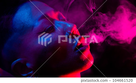 Asian woman with short haircut smoking in neon light. close-up portrait.  104661520