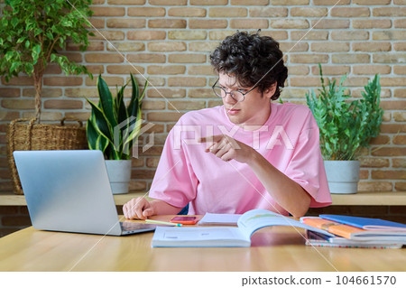 Guy student sitting at home with textbooks laptop, having online lesson 104661570