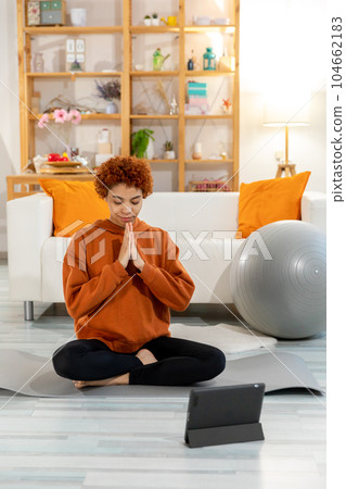 Yoga mindfulness meditation. Young healthy african girl practicing yoga at home. Woman sitting in lotus pose on yoga mat eyes close hands in prayer meditating indoor. Girl doing breathing practice Yoga mindfulness meditation. Young healthy african girl practicing yoga at home. Woman sitting in lotus pose on yoga mat eyes close hands in prayer meditating indoor. Girl doing breathing practice 104662183