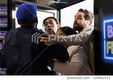 Crazy mad people shoppers pushing and shoving each other while trying to break into retail store on Black Friday, fighting with security guard. Crowd control in retail concept Crazy mad people shoppers pushing and shoving each other while trying to break into retail store on Black Friday, fighting with security guard. Crowd control in retail concept 104662431