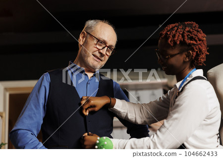 Elderly gentleman happy with perfect fit of bespoke suit vest made by professional meticulous suitmaker. Client satisfied with precise craftmanship done by expert couturier Elderly gentleman happy with perfect fit of bespoke suit vest made by professional meticulous suitmaker. Client satisfied with precise craftmanship done by expert couturier 104662433