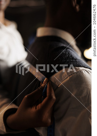 Extreme close up of meticulous skilled tailor taking sartorial stylish garment measurements on client. Seamstress manufacturing custom made refined premium quality business suit in atelier shop 104662476