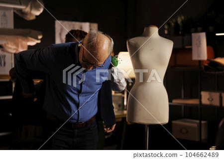 Elderly gentleman trying on premium quality bespoke garment, helped by professional seamstress. Senior client wearing custom handmade suit blazer made by expert couturier 104662489