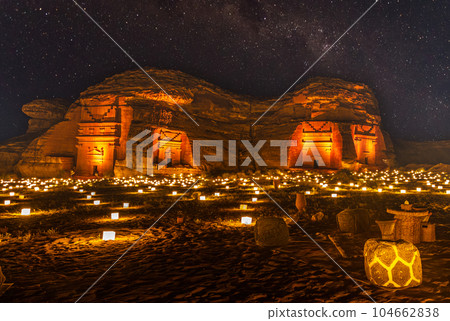 Starlight sky over the ancient nabataean tombs of Hegra city illuminated, night panorama, Al Ula, Saudi Arabia 104662838