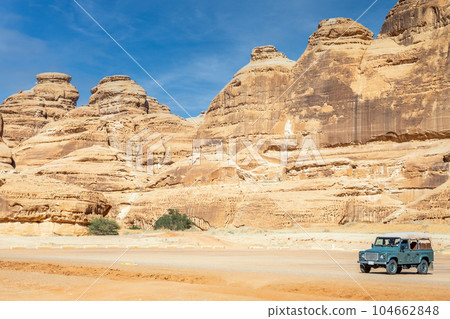 Off-road car and desert cliffs formations landscape at Hegra, Al Ula, Saudi Arabia Off-road car and desert cliffs formations landscape at Hegra, Al Ula, Saudi Arabia 104662848