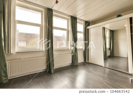 an empty room with wood floors and green drapes on the window is open to let light into the room 104663542