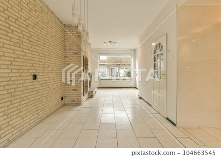a long hallway with white tile on the floor and beige brick wall behind it, there is an open door that leads to another a long hallway with white tile on the floor and beige brick wall behind it, there is an open door that leads to another 104663545