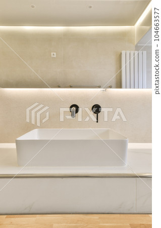 a modern bathroom with wood flooring and white walls, along with an illuminated mirror on the wall above it 104663577