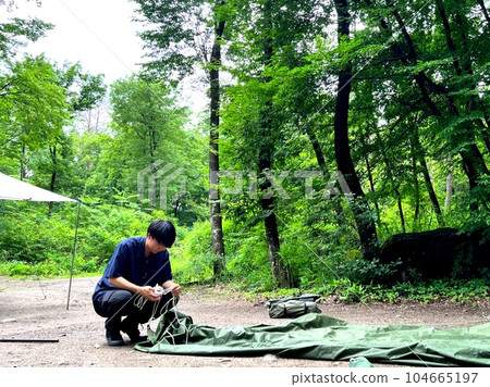A young man preparing to set up a solo camp tarp 104665197