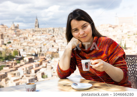 Portrait of female tourist drinking coffee at table overlooking Toledo, Mirador del Valle, Spain Portrait of female tourist drinking coffee at table overlooking Toledo, Mirador del Valle, Spain 104666280