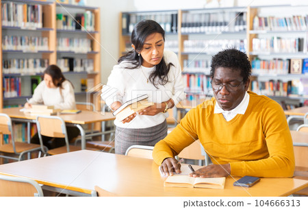 Latin american woman offering books to aframerican man in library Latin american woman offering books to aframerican man in library 104666313