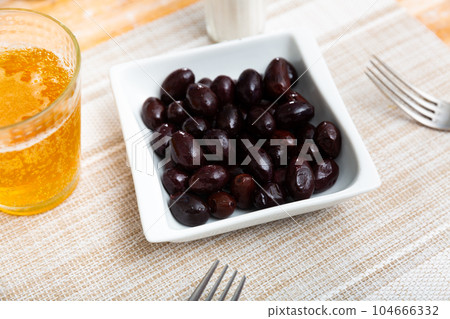 On square white plate lies portion of large ripe black olives with stone. On square white plate lies portion of large ripe black olives with stone. 104666332