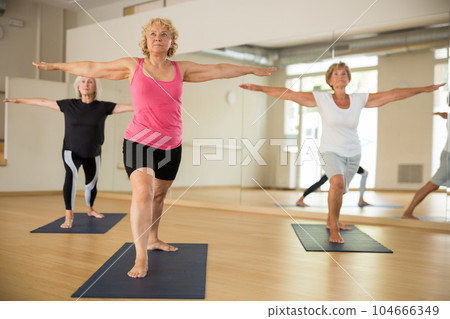 Three mature women perform the exercise by taking the warrior pose II Three mature women perform the exercise by taking the warrior pose II 104666349