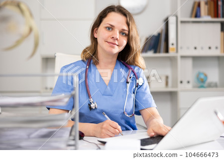 Portrait of positive woman doctor sitting at table 104666473