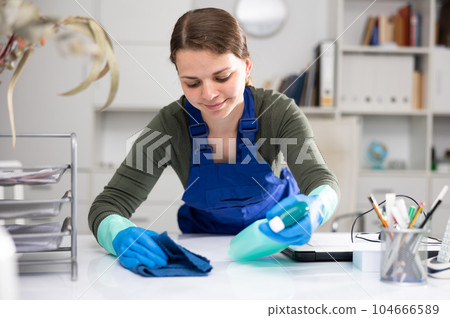 Woman in an overalls cleans the table at office Woman in an overalls cleans the table at office 104666589
