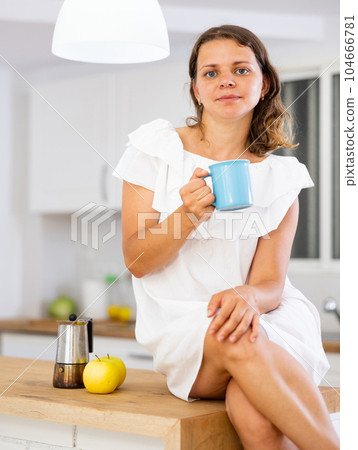 Woman drinking coffee in kitchen at home 104666781