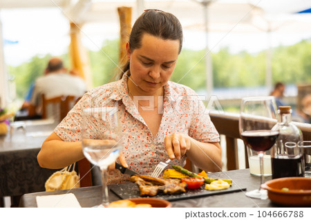Woman eating hot dish of lamb in restaurant on an outdoor terrace Woman eating hot dish of lamb in restaurant on an outdoor terrace 104666788