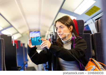 Interested female traveler filming landscapes behind glass in express train 104666930