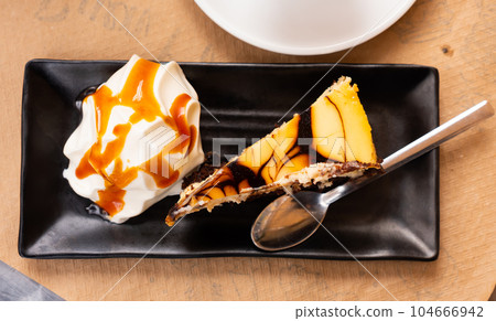 On black plate is thin slice of cheesecake with ball of ice cream with caramel sauce 104666942