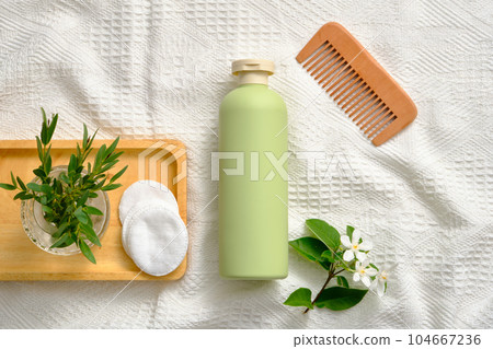 Pastel bottle without label arranged with wooden comb and a tray of green leaves vase and some cotton pads. Cosmetics, products for care and personal hygiene concept Pastel bottle without label arranged with wooden comb and a tray of green leaves vase and some cotton pads. Cosmetics, products for care and personal hygiene concept 104667236