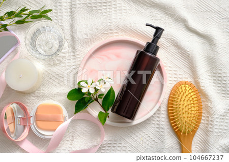 Unlabeled pump bottle placed on marble tray with white flowers. A brush, cushion compact, scented candle and a glass of water displayed. Cleansing product advertising Unlabeled pump bottle placed on marble tray with white flowers. A brush, cushion compact, scented candle and a glass of water displayed. Cleansing product advertising 104667237