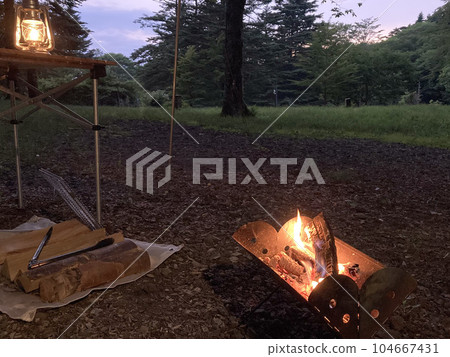 Bonfire, lantern and lots of firewood in the evening forest 104667431