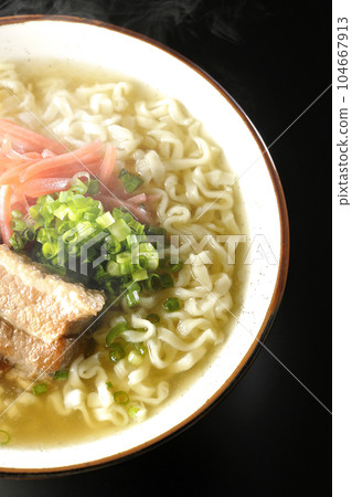 A bird's-eye view of hot Okinawa soba with pork ribs, plenty of small green onions, and red ginger on a black background 104667913
