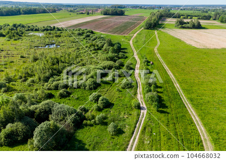 A view from a height of a country road receding into the distance running between green fields A view from a height of a country road receding into the distance running between green fields 104668032