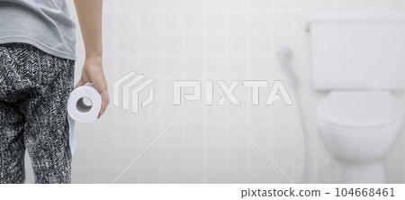 A person suffering from diarrhea holds a roll of toilet paper in front of the toilet bowl A person suffering from diarrhea holds a roll of toilet paper in front of the toilet bowl 104668461