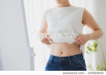 Woman checking her stomach in the mirror Woman checking her stomach in the mirror 104669008