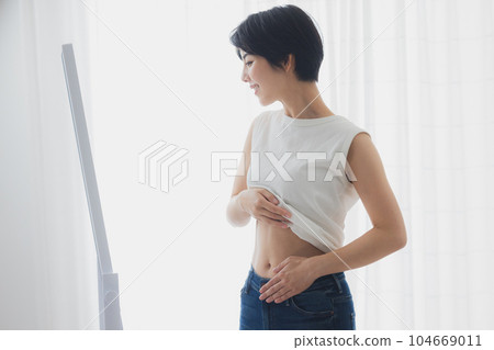 Woman checking her stomach in the mirror Woman checking her stomach in the mirror 104669011