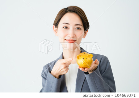 A young woman holding a piggy bank and pointing at it Business image 104669371