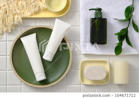 Top view, flat lay of cosmetic bottles on round plate, decorated with towel, scented candles and soap on white ceramic background. Mockup scene for advertising with bathroom concept 104671722