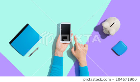 Person using smartphone with piggy bank Person using smartphone with piggy bank 104671900