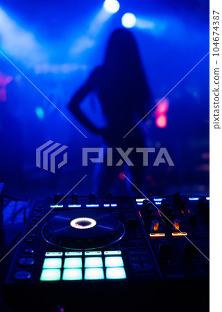 silhouette of young slim dancers on stage out of focus through the DJ booth and a mixer 104674387