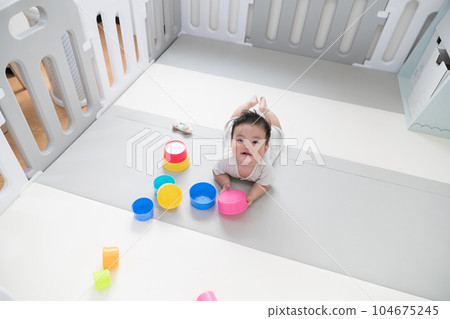 A happy 8-month-old baby playing with an educational toy on a play mat in the living room with natural light A happy 8-month-old baby playing with an educational toy on a play mat in the living room with natural light 104675245