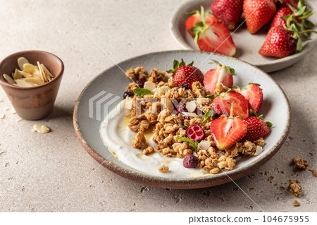 Healthy breakfast: fresh granola, muesli with yogurt, strawberry and honey on beige textured background. Copy space Healthy breakfast: fresh granola, muesli with yogurt, strawberry and honey on beige textured background. Copy space 104675955