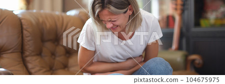 Woman sitting on sofa and touching belly writhing in pain 104675975