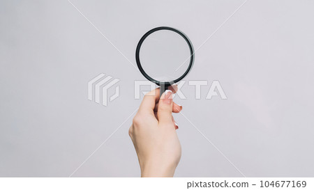 Searching loupe. Detective glass. Female hand reading copy space for text with magnifying tool isolated on gray background. 104677169