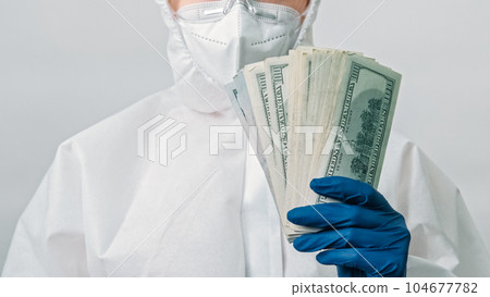 Healthcare insurance. Medical costs. Unrecognizable doctor in white protective coverall with dollars money fan in hand in glove isolated on grey background. 104677782