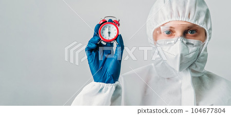 Timely diagnosis. Virus specialist. Female woman doctor in medical protective equipment with alarm clock isolated on grey background empty space. 104677804